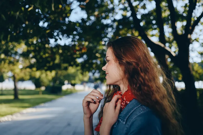 lifestyle woman in modern boho-western denim street style with red bandana outdoors, film color, natural light, casual summer look, green park background