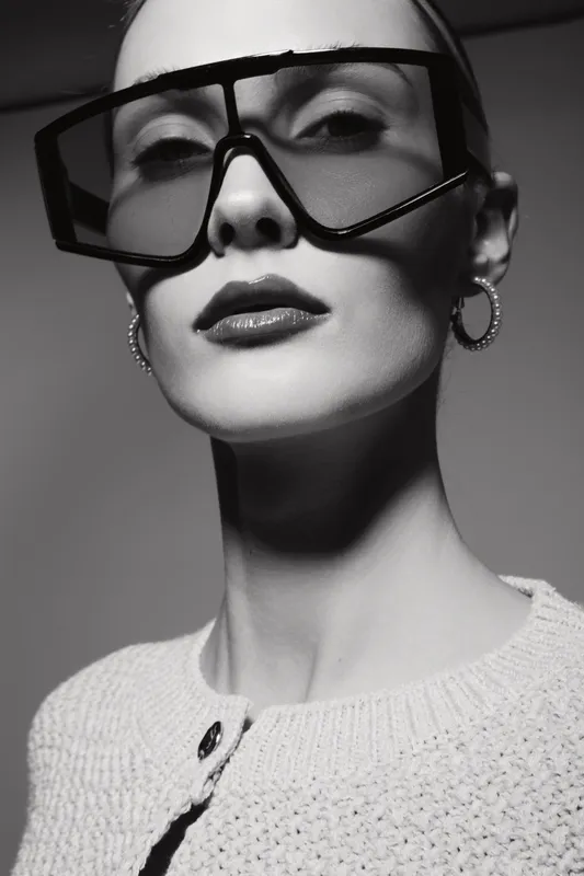 Elegant caucasian woman with pale skin wearing large fashion glasses and hoop earrings poses in studio in monochrome. Concept of style and modern beauty.