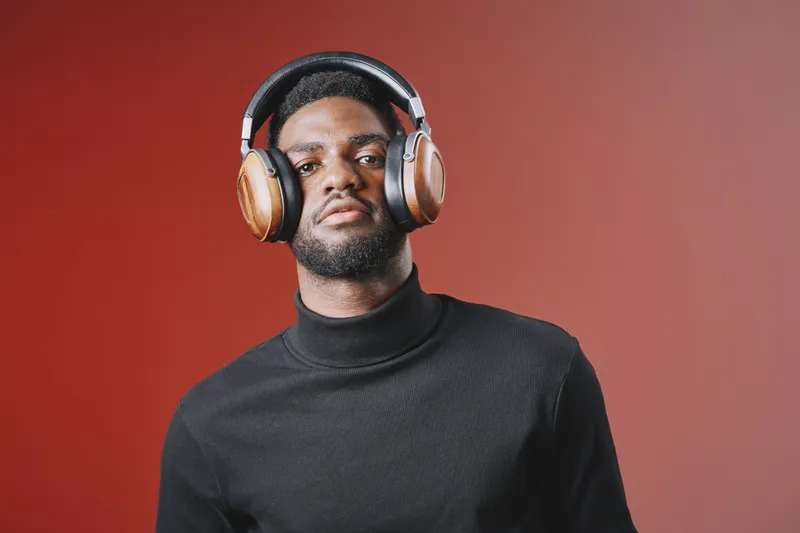 Stylish African American man wearing headphones with a confident expression, set against a warm red background, exemplifying modern music culture and lifestyle