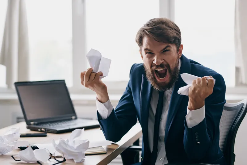 Бизнесмены работают за ноутбуком в офисе, испытывая эмоции недовольства от технологий