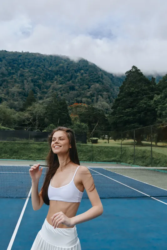 Young female tennis player celebrating victory on the court, wearing sporty attire, against a scenic mountain backdrop with a vibrant color palette