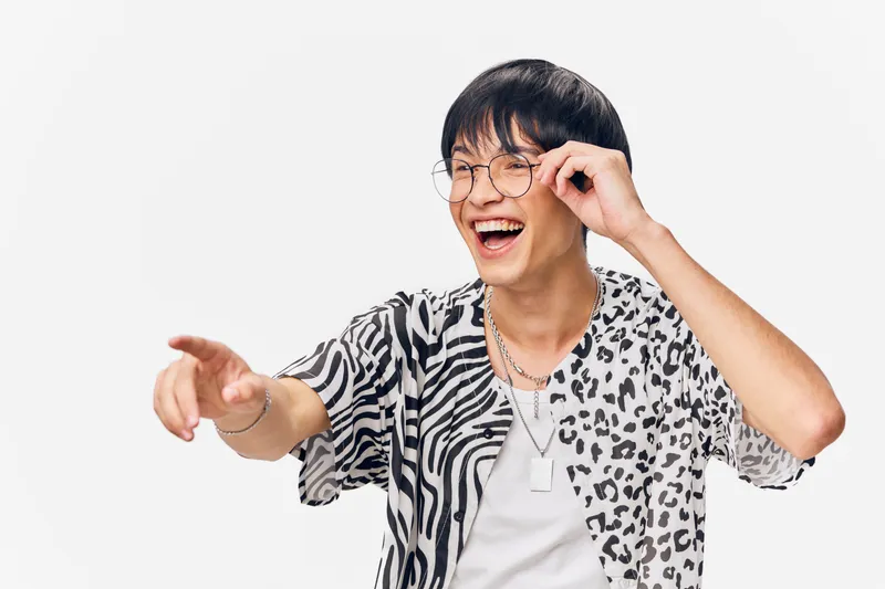 laughing man wearing glasses and animal print shirt pointing forward with joyful expression on white background, stylish casual clothing and happy mood