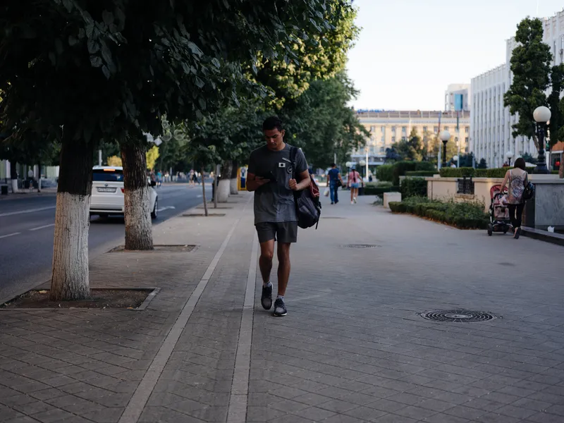 Мужчина идёт по улице на природе рядом со зданиями в городе