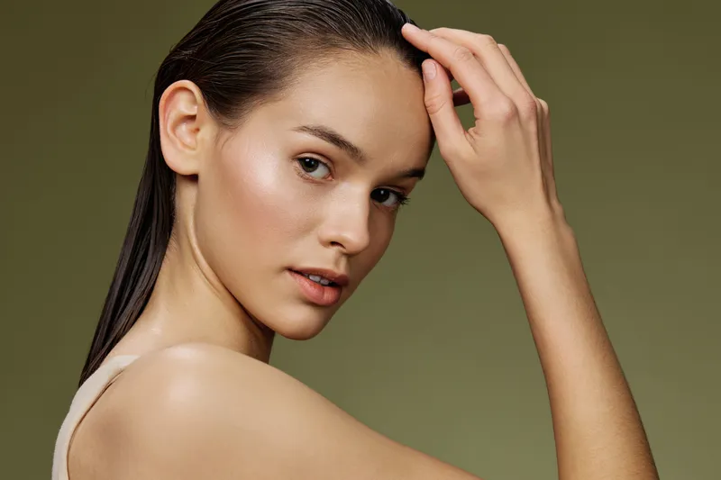 Elegant young model with wet hair and natural makeup, showcasing a serene expression against a soft green background, perfect for beauty campaigns and skin care products