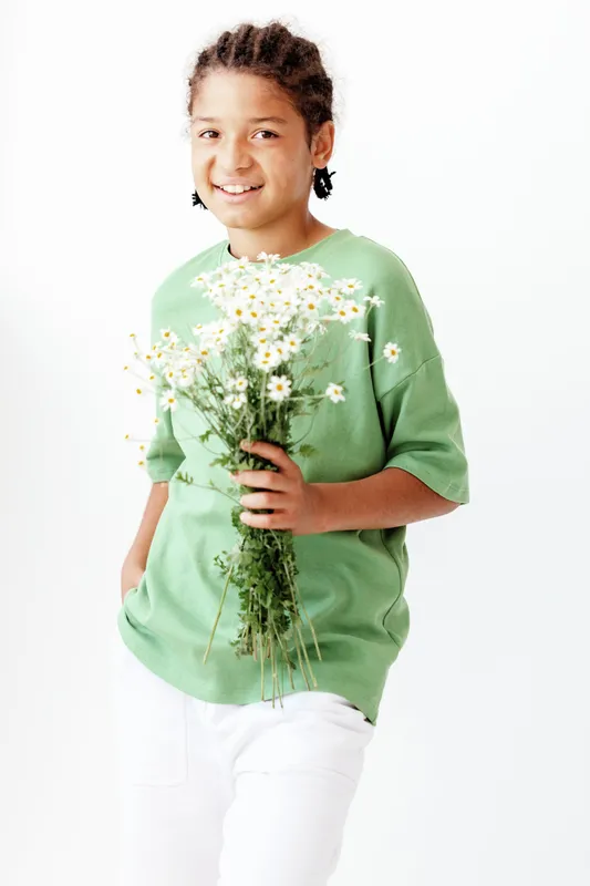 Радостный маленький мальчик стоит и улыбается, держа букет ромашек на фоне простого белого фона