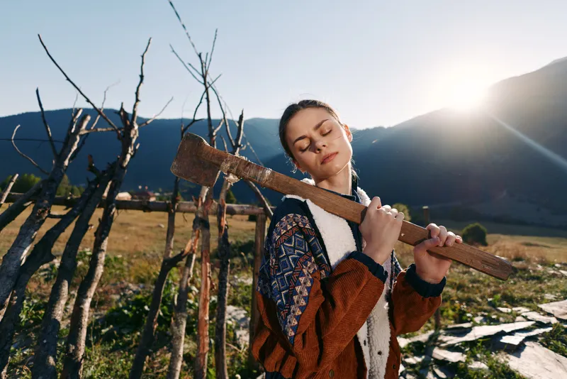 Woman rural portrait carrying a wooden plank on her shoulder near a rustic fence in the mountains at sunset, eyes closed in nature, outdoor countryside lifestyle and serene moment.