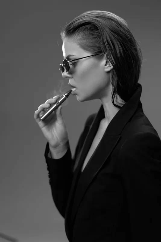 Profile of a stylish woman vaping in black jacket and sunglasses in black and white