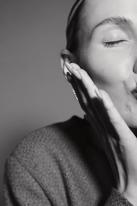 Close-up of a light skinned Caucasian woman with closed eyes touching her face gently. Concept of skin care, tenderness, and natural beauty in black and white portrait.