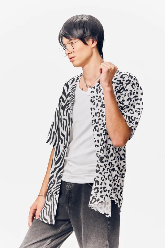 young man wearing casual animal print shirt and glasses posing thoughtfully against white background with relaxed confidence and stylish modern look