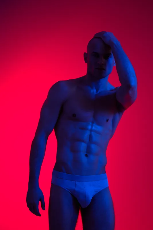 Athletic man posing with a confident expression against a colorful backdrop, showcasing a blend of vibrant shades that emphasize his physique.