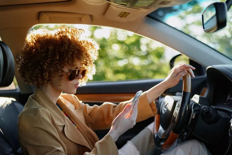 Woman driving a car with curly hair and sunglasses, sunlit interior, retro film color, relaxed lifestyle moment on the road, soft breeze and warm glow, candid joyful atmosphere for everyday travel