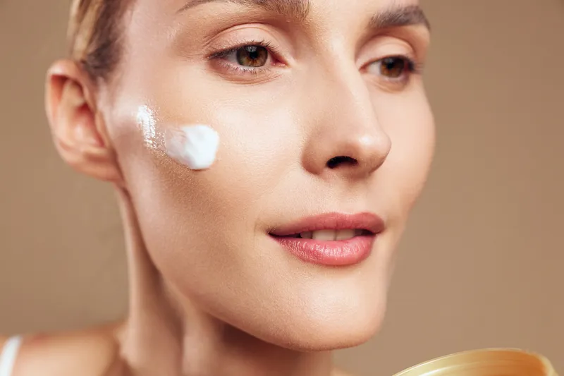 Close up of woman applying cream on face, smooth skin texture, natural makeup, soft lighting, skincare routine, healthy complexion, neutral background