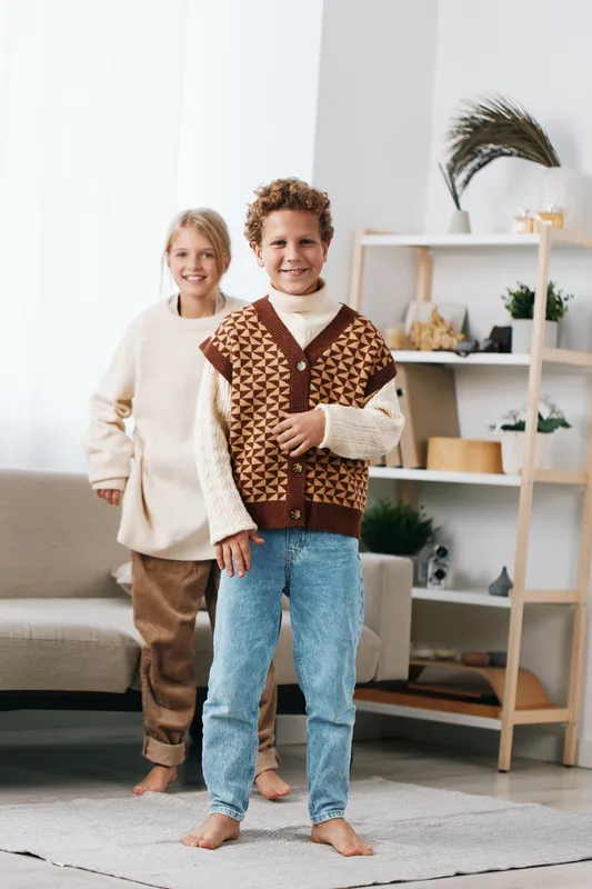 Authentic lifestyle scene shows children indoors in cozy knitwear and sweaters, capturing a playful moment with genuine charm and a warm, everyday vibe.