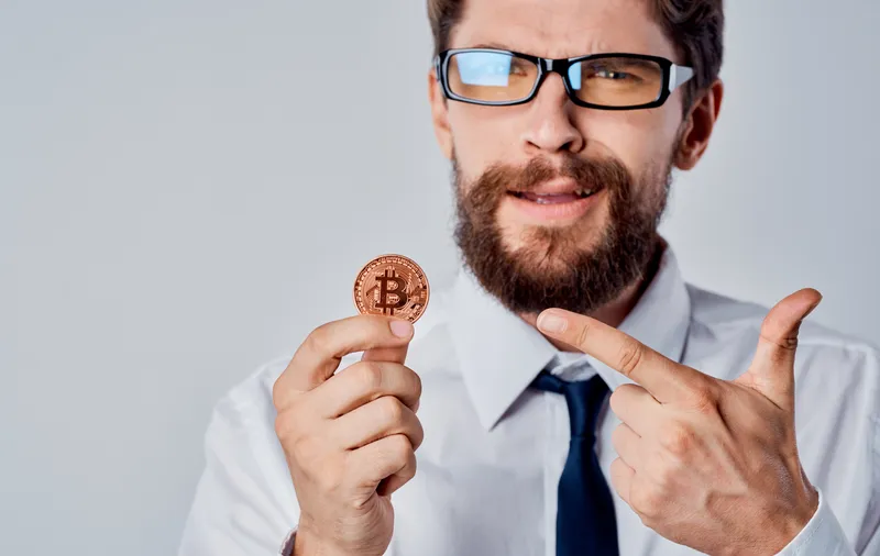 Весёлый мужчина с золотой монетой, биткоином и криптовалютой в контексте финансов