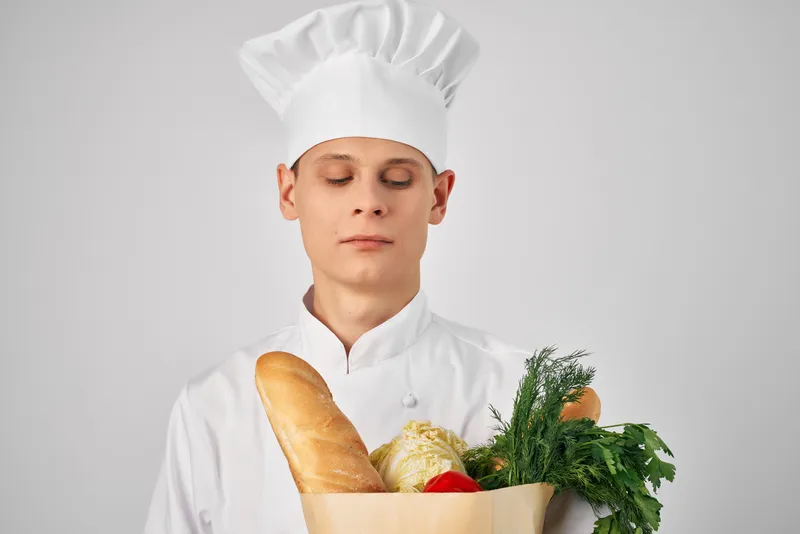 Мужчина в одежде шеф-повара с упаковкой продуктов готовит еду на кухне