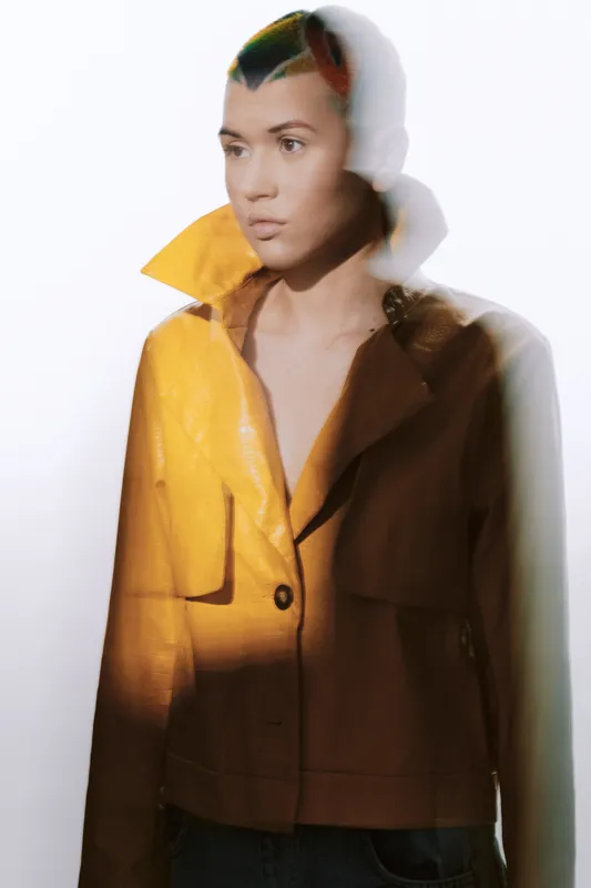 young woman in yellow jacket standing with blurred double exposure effect against white background, artistic fashion portrait in modern style