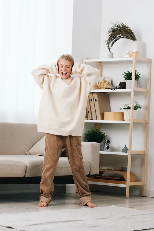 Authentic playful lifestyle scene featuring a cheerful child in a cozy home, dressed in oversized sweater and soft pants, capturing daily play and comfort.