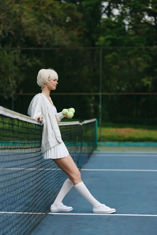 Elegant female tennis player in white attire holding tennis balls, showcasing a confident expression on blue court background