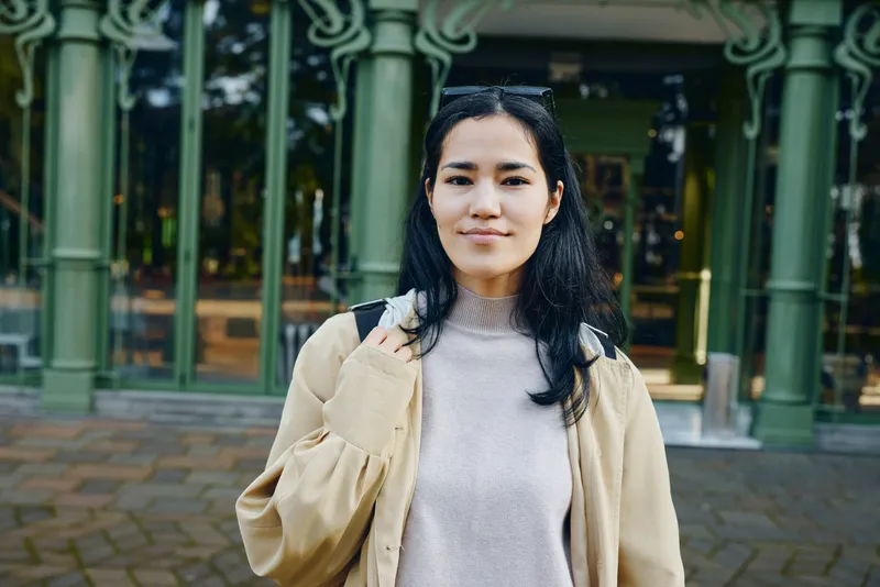 Woman outdoors in casual clothing near green architectural columns in daytime urban setting, calm expression, street style and confident vibe, approachable appearance