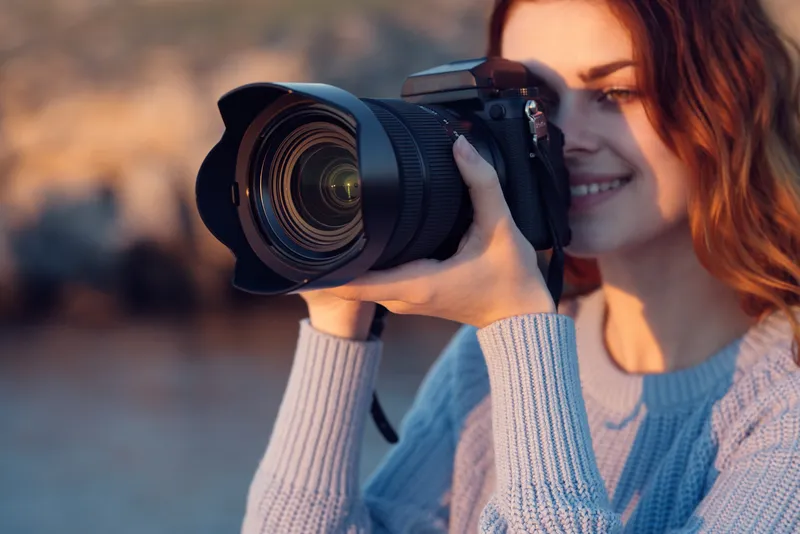 Красивая рыжеволосая женщина с фотоаппаратом на природе в горах возле реки