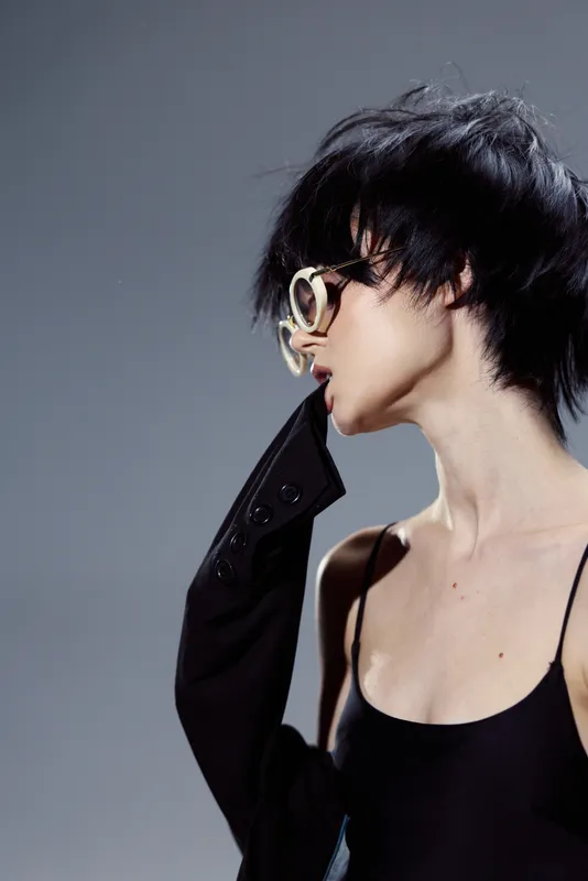 Stylish woman with sunglasses and short hair wearing black outfit in moody lighting