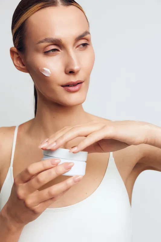 Close-up of a woman applying cream to her face in a bright studio, illustrating a simple skincare routine, hydration, and healthy glow in a calm beauty moment.