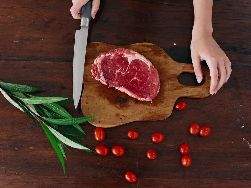 Женщина с ножом в руке нарезает свежее мясо стейка для жарки на кухне