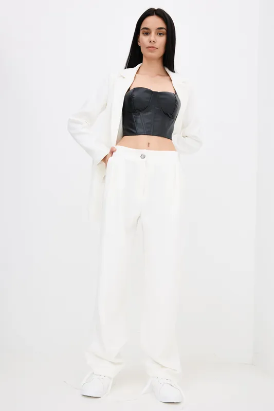 woman in white pantsuit and black corset top posing confidently with hands in pockets against minimalist white background, modern fashion style and monochrome palette