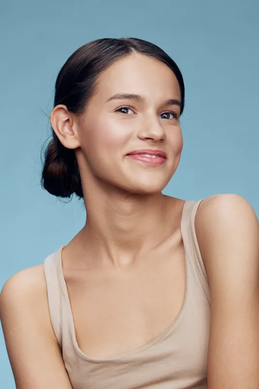 Young woman with clear skin smiling against a blue background, showcasing a natural beauty concept, perfect for health and skincare themes