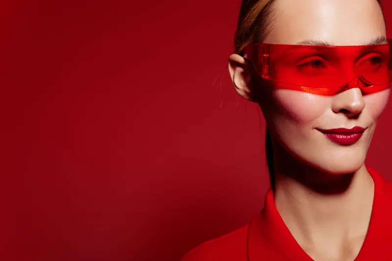 Close-up of a confident woman wearing red sunglasses and red clothing against a red background. Concept of fashion, style, modern look, and bold color contrast.