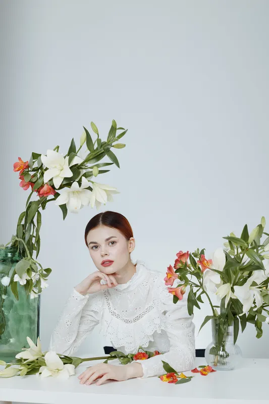 Elegant young woman in white blouse surrounded by blooming flowers, showcasing beauty and serenity in a soft pastel color palette, perfect for seasonal marketing