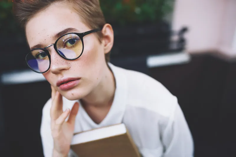 Образованная женщина в очках с книгой сидит за столом