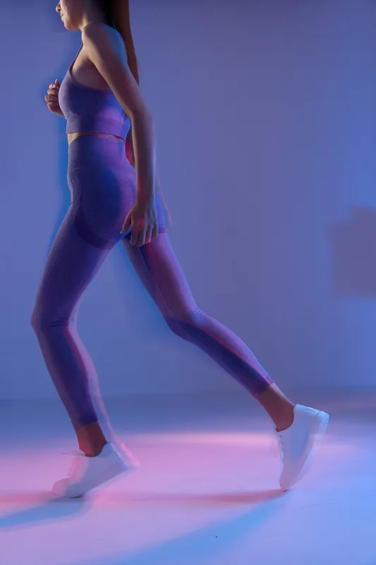 Woman sport fitness in purple activewear walking in futuristic neon lighting, showcasing strength, balance, and dynamic motion indoors.