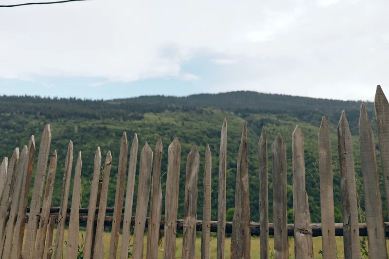Fence wooden countryside landscape hills forest rural sky nature rustic scene with weathered picket boards in foreground distant green tree covered slopes and cloudy blue sky