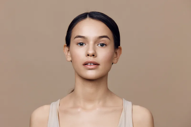 Young female model with natural makeup, neutral beige background, conveying calmness and confidence, suitable for beauty and wellness themes