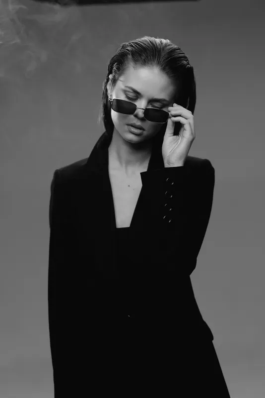 Black and white portrait of a stylish woman wearing sunglasses and a dark blazer with wet hair.