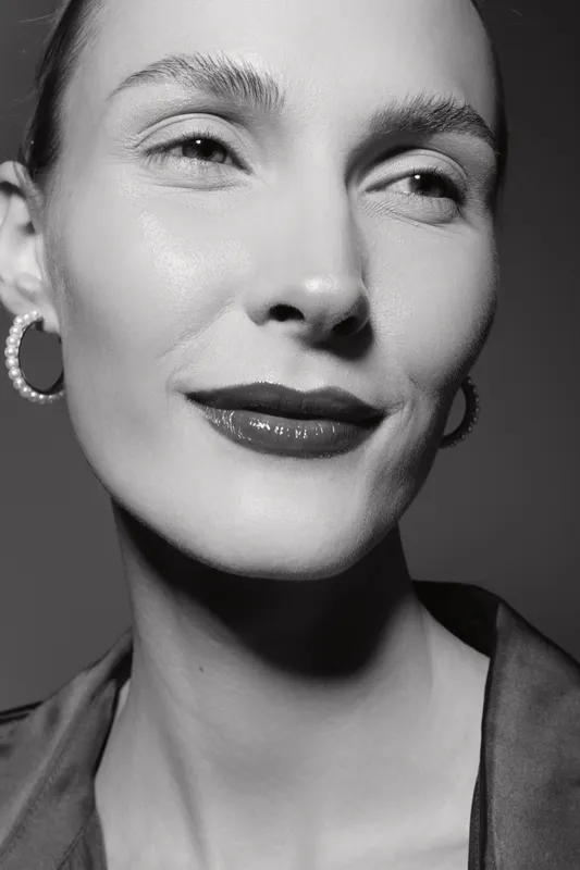 Close-up portrait of a smiling Caucasian woman with light skin and hoop earrings in black and white studio lighting.