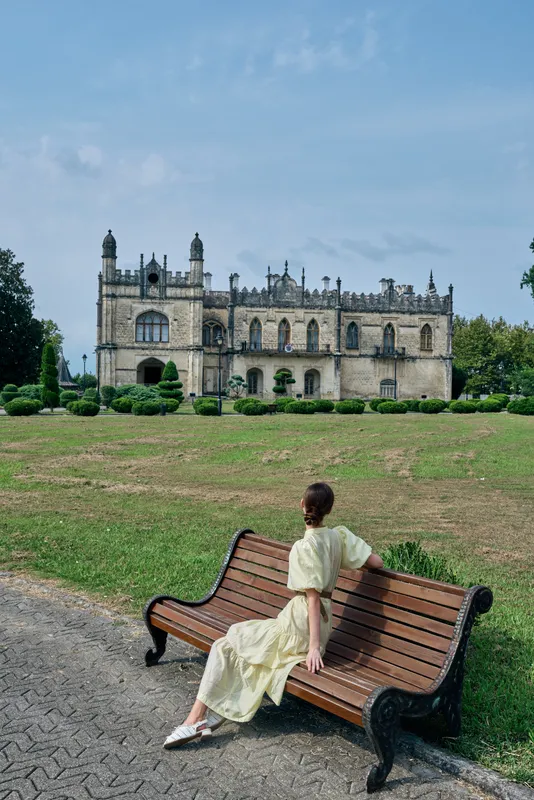 woman on bench in park facing historic manor, dress flowing, architecture detailed, grass and path, solitude moment with authenticity inclusivity, serene relaxed portrait