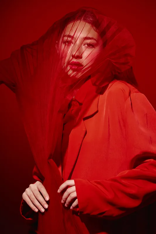 Fashion model in vibrant red coat and gloves with red veil. Close-up portrait with dramatic lighting and intense gaze. Concept for beauty, style, and creative fashion editorial.