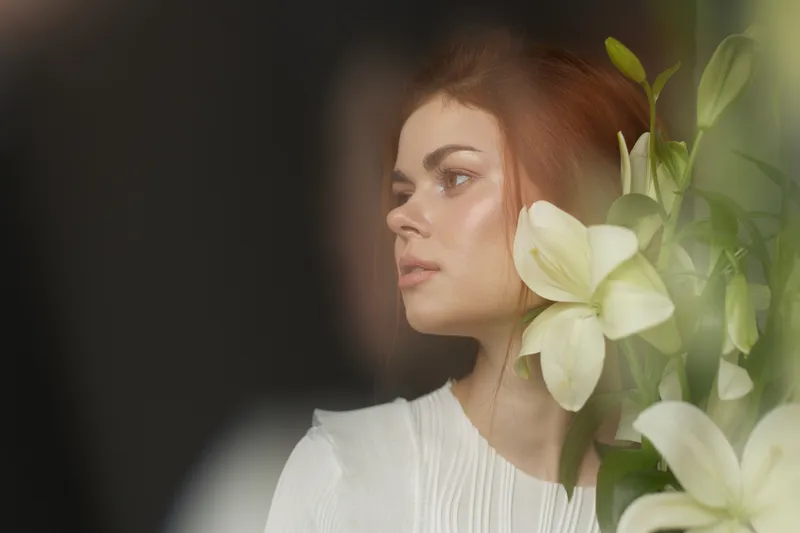 Portrait of a young woman with red hair, wearing a white blouse, surrounded by white flowers, evoking feelings of beauty and serenity in a soft and delicate ambiance