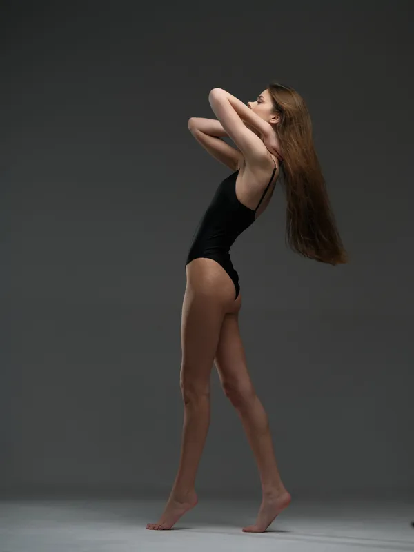 graceful woman posing in black bodysuit with long hair, minimalist studio background, elegant posture