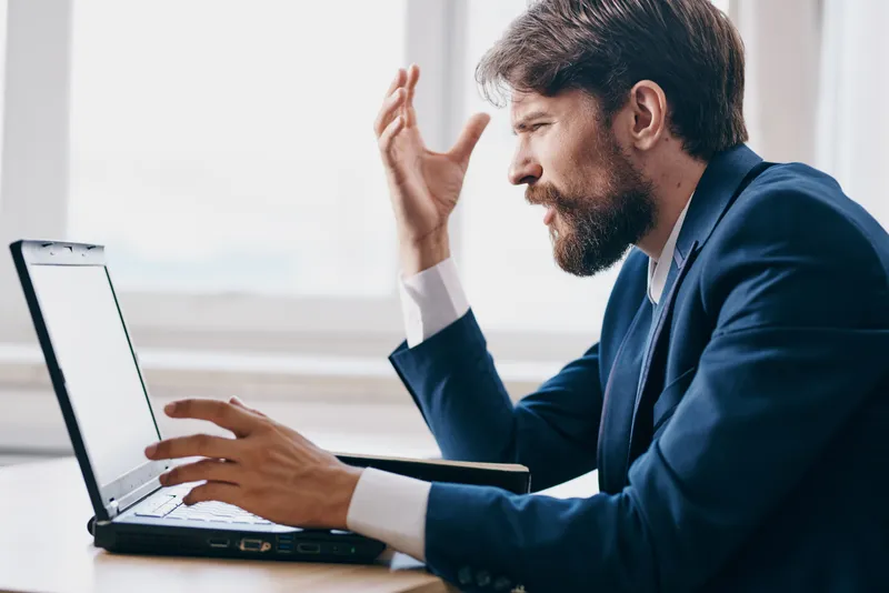 Бизнесмены работают за ноутбуком в офисе, на их лицах видны эмоции