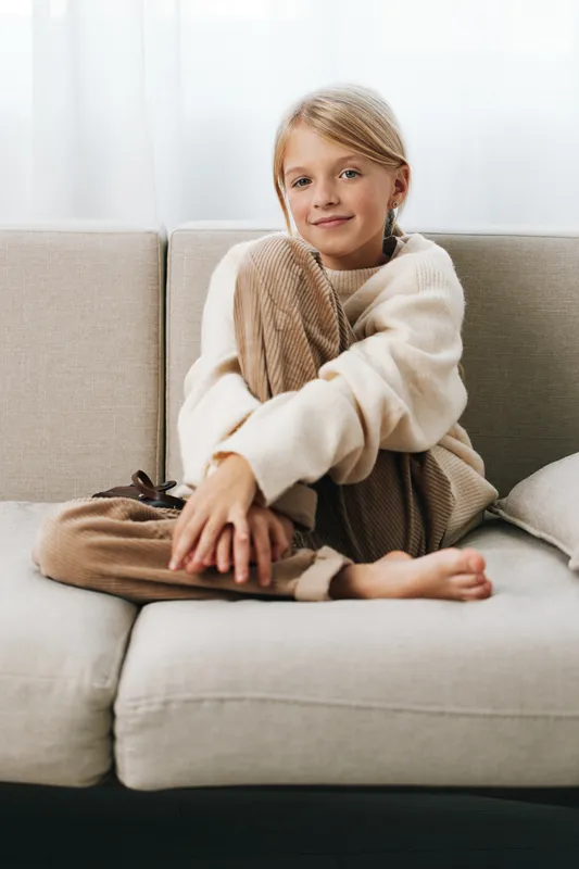 Authenticity shines in a cozy home scene as a child sits on a sofa in soft knitwear. A candid lifestyle moment that hints at play, school, and everyday life.
