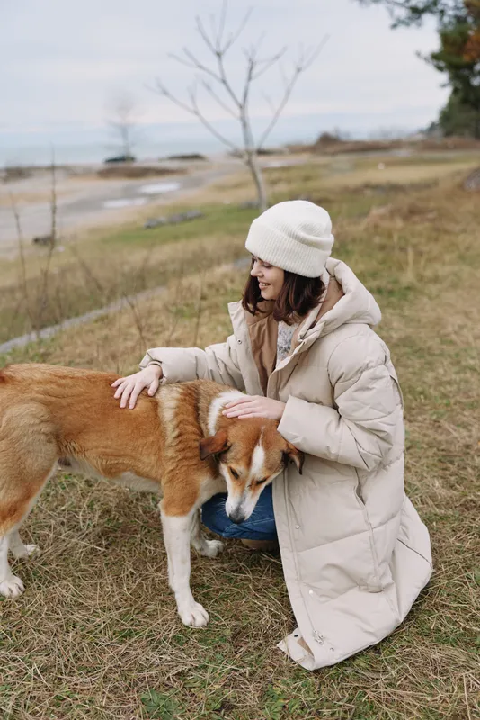 Dog, petting, woman, outdoor, winter, park, a woman in a warm coat kneels to pet a friendly dog on a grassy field under a calm sky, capturing tender companionship.