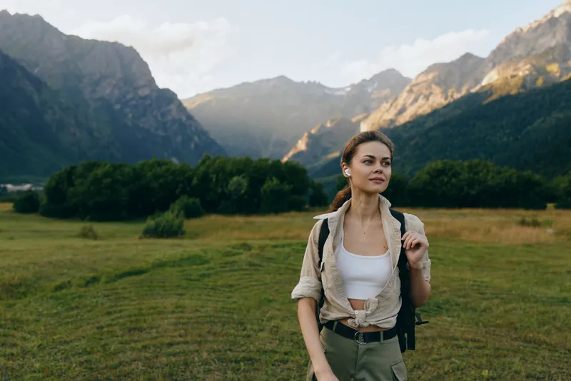 Woman with backpack exploring a landscape valley and mountains, outdoors in nature, hiking and adventure lifestyle in a meadow scene, smiling and confident.