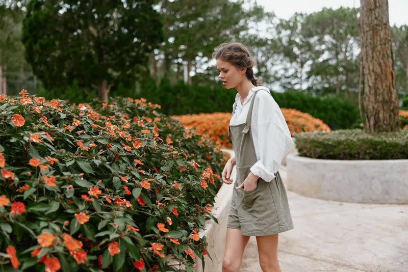 A young woman in an olive green dress enjoys a vibrant flower garden, evoking a feeling of tranquility and connection with nature