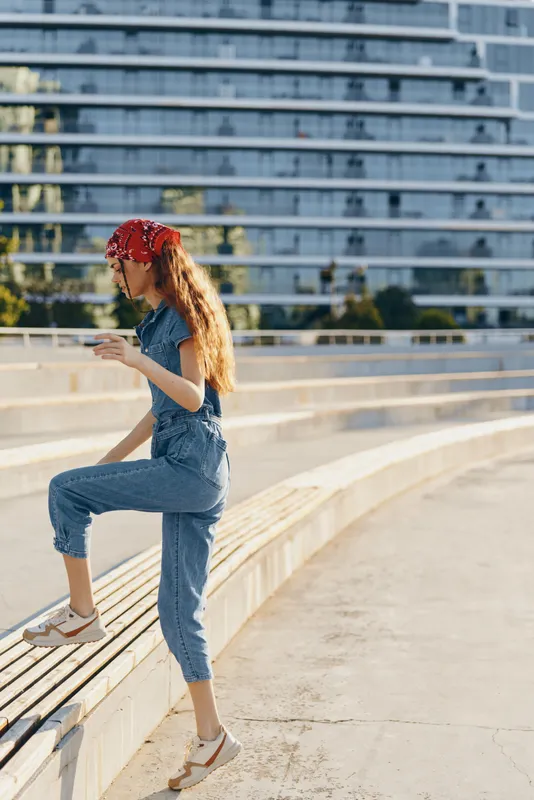 Lifestyle woman in modern boho-western denim street style with a red bandana, casual shoes, and natural light film color, captured in a dynamic urban outdoor scene.