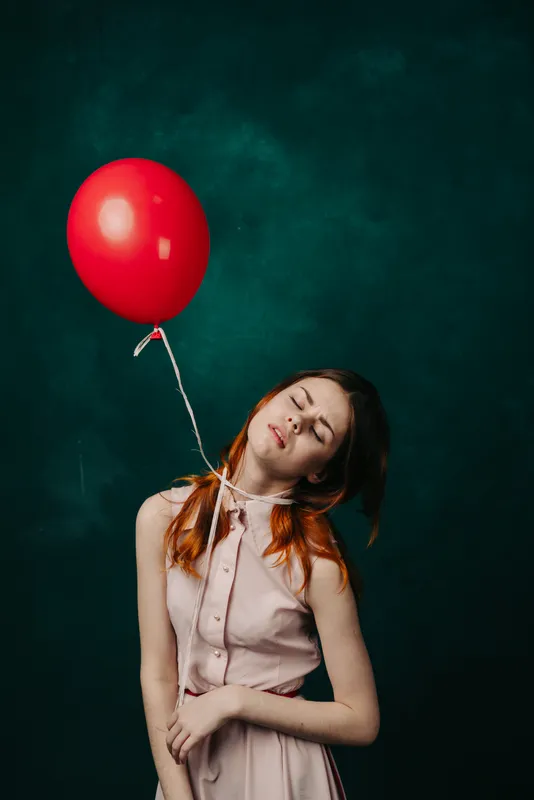 Женщина в розовом платье держит в руках надувной мяч на зелёном фоне