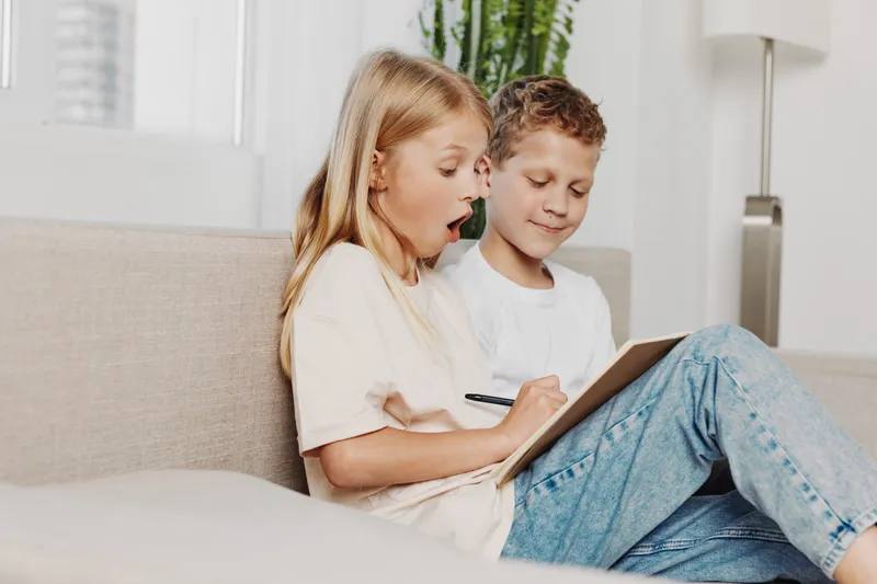 Two children sitting on a couch interact with a tablet, the girl showing surprise while the boy smiles quietly. Concept for technology, learning, and childhood interaction.