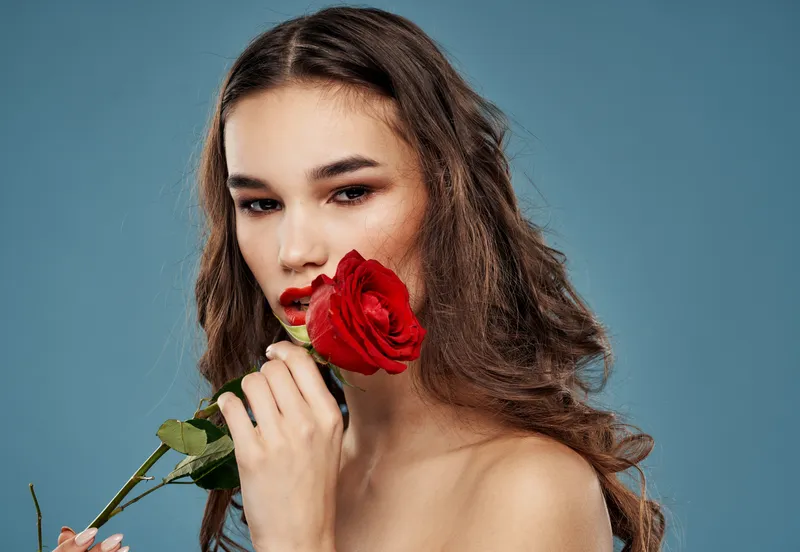 Женщина с розой в зубах, вечерний макияж, синий фон, модель